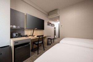 Une chambre d’hôtel équipée d’un lit, d’un bureau avec une chaise, d’un petit réfrigérateur, d’une machine à café, d’un téléviseur à écran plat et d’un climatiseur fixé au mur.