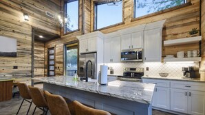 A modern kitchen with white cabinets, a granite countertop, and a bar area with stools. - These Are The Days | Luxury Hochatown Cabin with Hot Tub, Grill & Pet-Friendly Comfort (Hochatown)