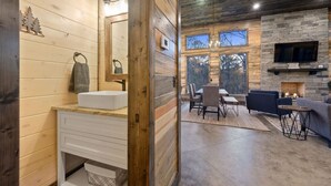 A wooden cabin interior with a bathroom, dining area, and fireplace. - These Are The Days | Luxury Hochatown Cabin with Hot Tub, Grill & Pet-Friendly Comfort (Hochatown)