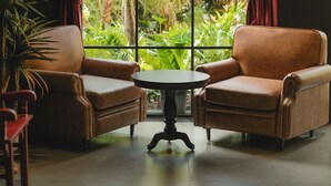 Ein Zimmer mit zwei Ledersesseln, einem kleinen runden Tisch und einem großen Fenster mit Vorhängen.