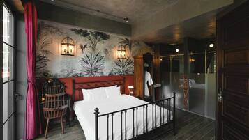 A bedroom with a bed, a nightstand, a lamp, a wall-mounted shelf, and a window with curtains.
