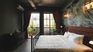Ein Schlafzimmer mit einem großen Bett, einem Nachttisch, einer Kommode und einem Balkon mit Pflanzen.