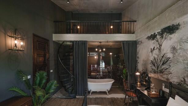 Ein geräumiges Zimmer mit einem großen Bett, einer Sitzecke mit einer Bank und Pflanzen, einer Treppe und einem Badezimmer mit einer Badewanne.