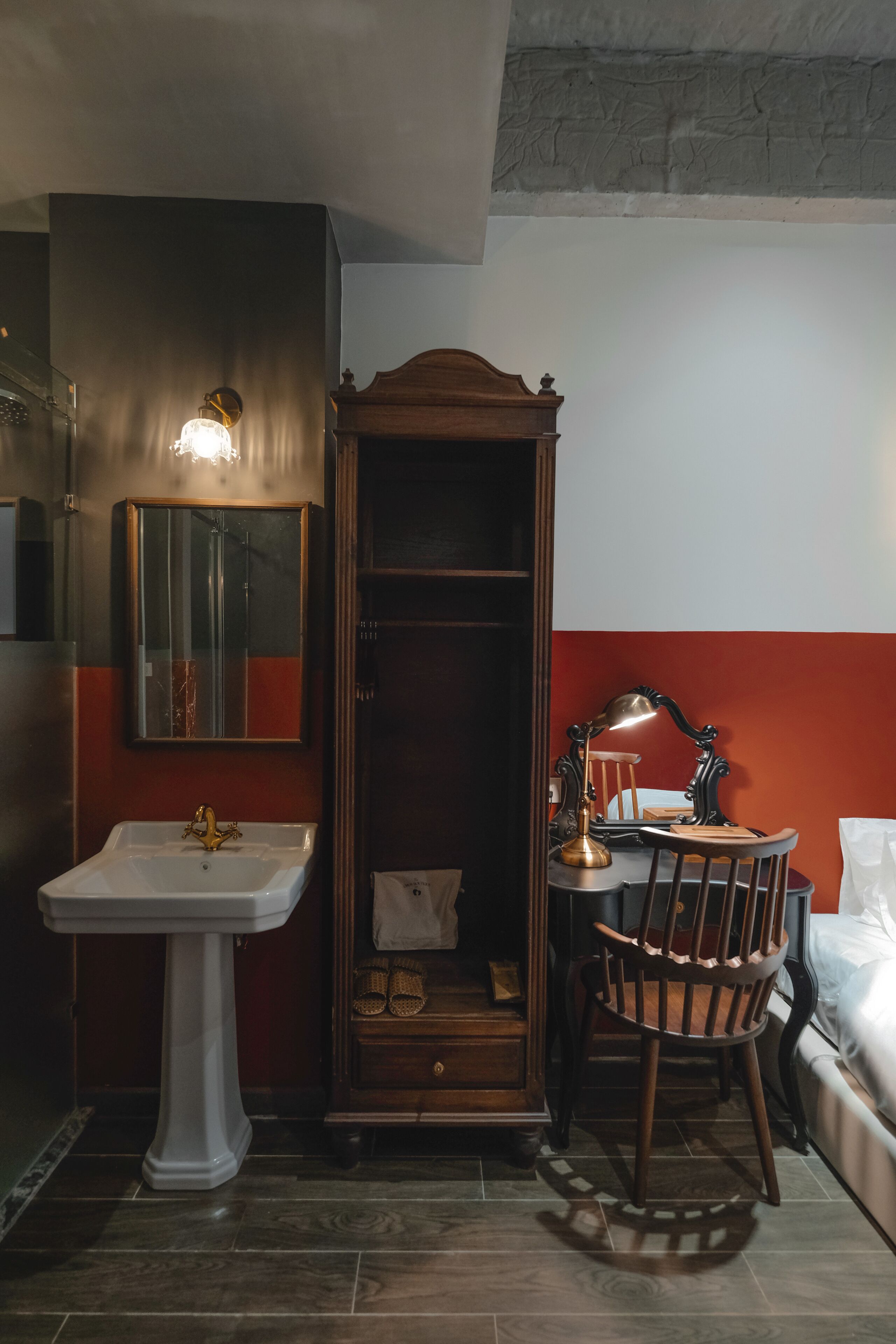Ein Badezimmer mit Waschtisch, Spiegel, Holzschrank, Stuhl und Bett.