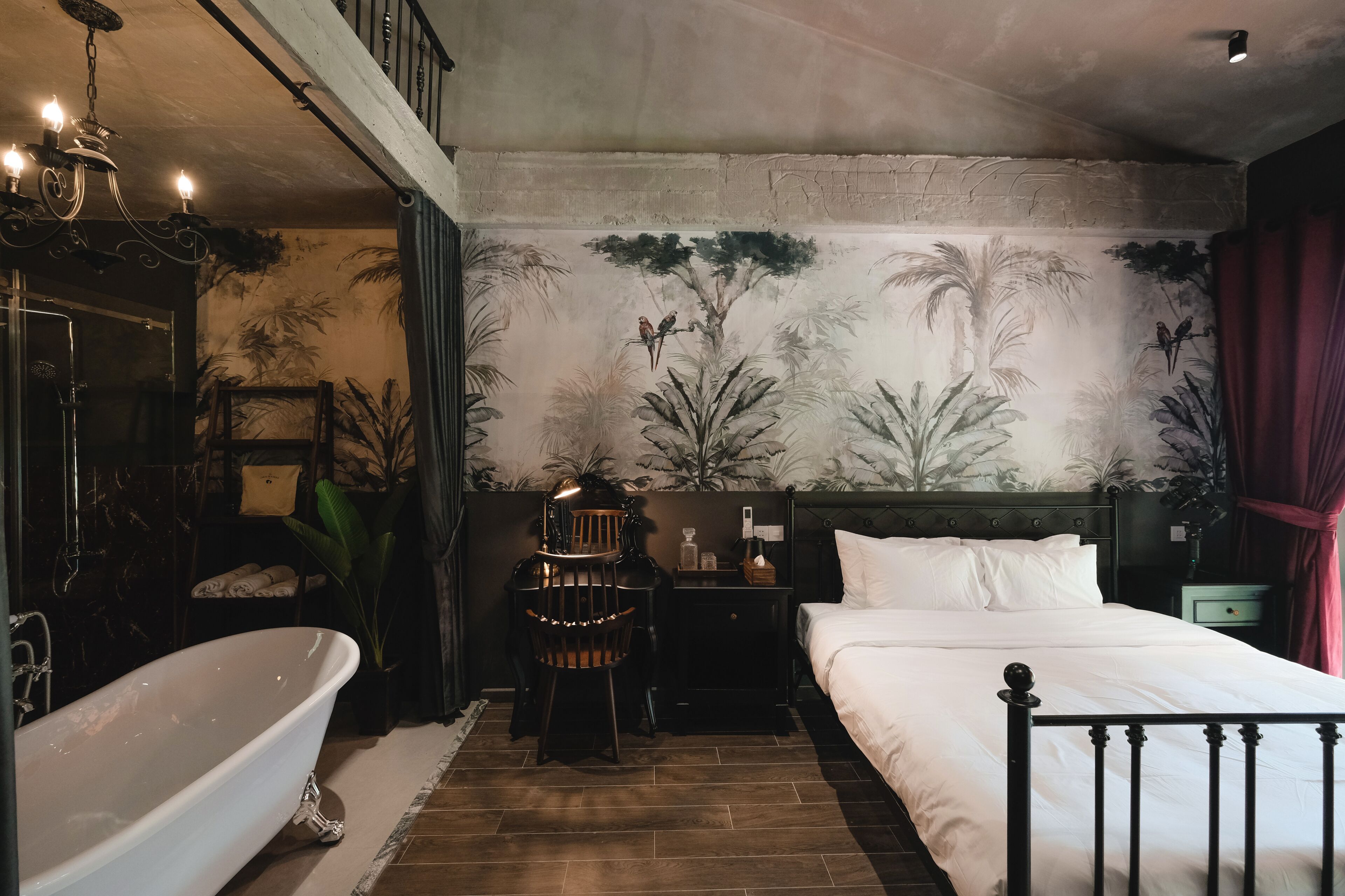 Un dormitorio con una cama grande, una zona de estar con una silla y una mesa, una bañera y un mural en la pared.