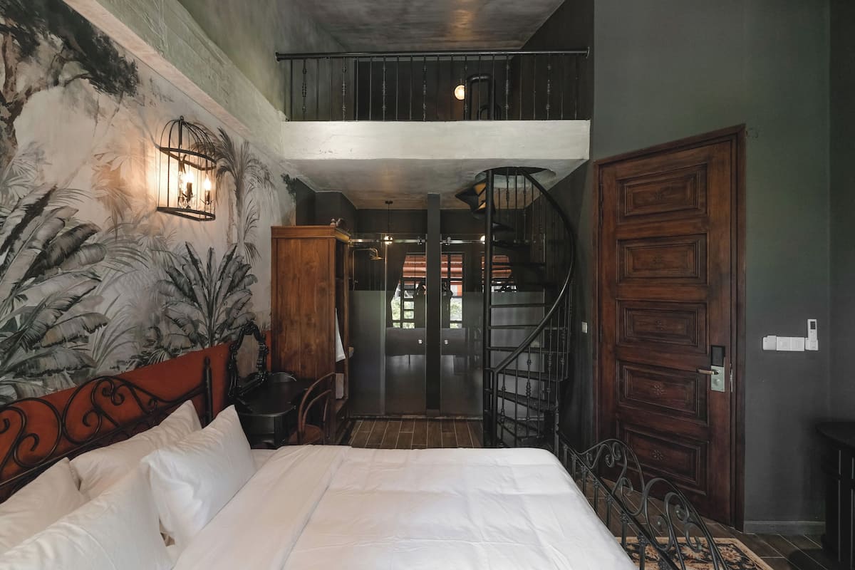 Un dormitorio con cama, mesita de noche, lámpara de pared, escalera y una puerta.