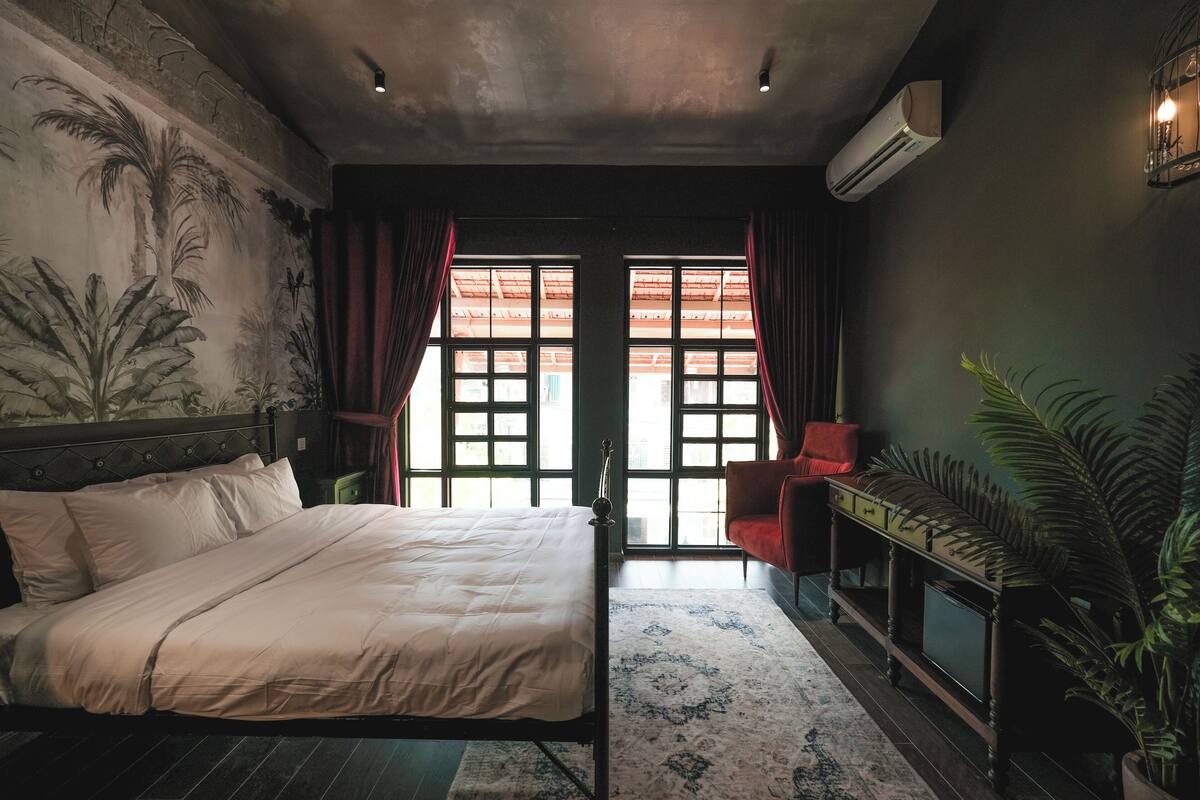 Un dormitorio con cama, escritorio, silla y una ventana grande con cortinas.