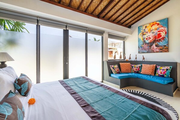 A modern bedroom with a large bed, a curved sofa, and a painting on the wall. - Romantica Villa with Private Pool (Ubud)