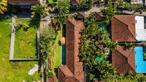 An aerial view of a resort with multiple bungalow-style buildings, a central swimming pool, and lush greenery.