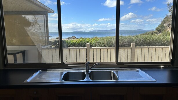A kitchen with a double sink and a view of the ocean and mountains through a large window. - Wilsons Prom Holiday Park (Yanakie)
