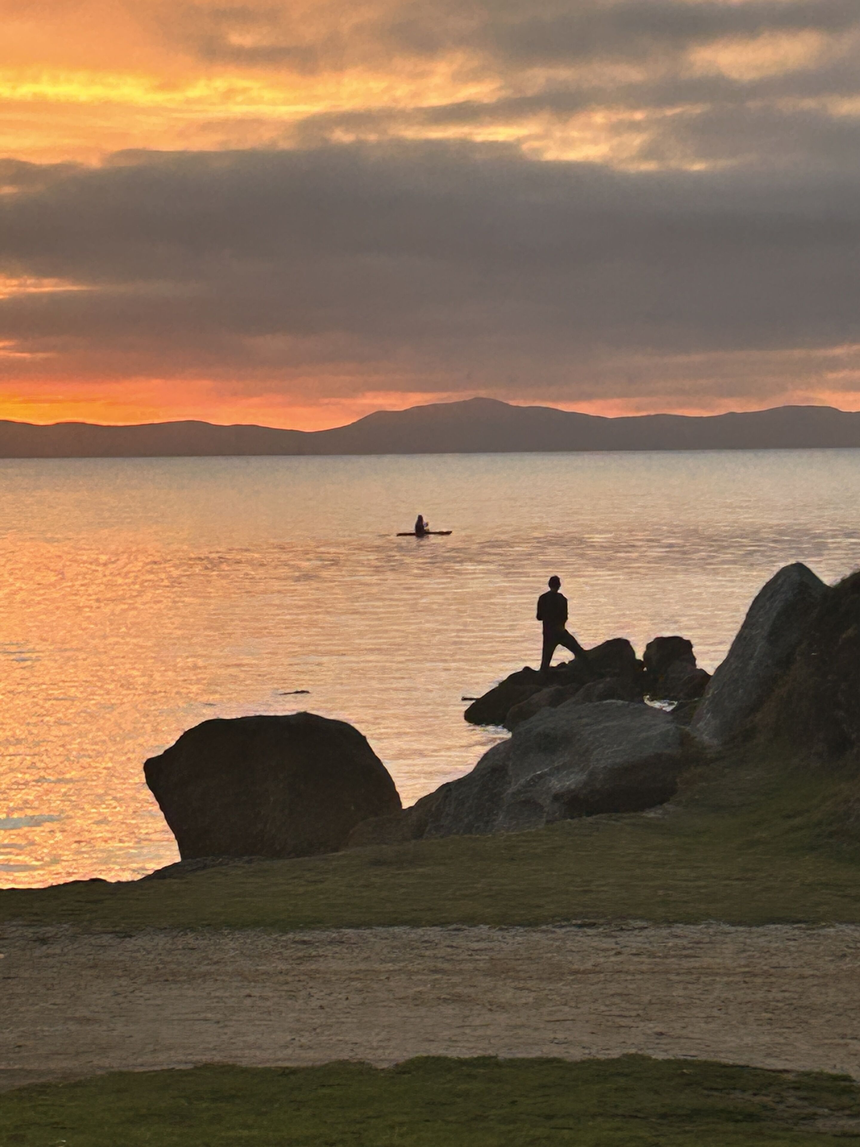 A coastal landscape with rocky outcrops and a person standing on a rock.
