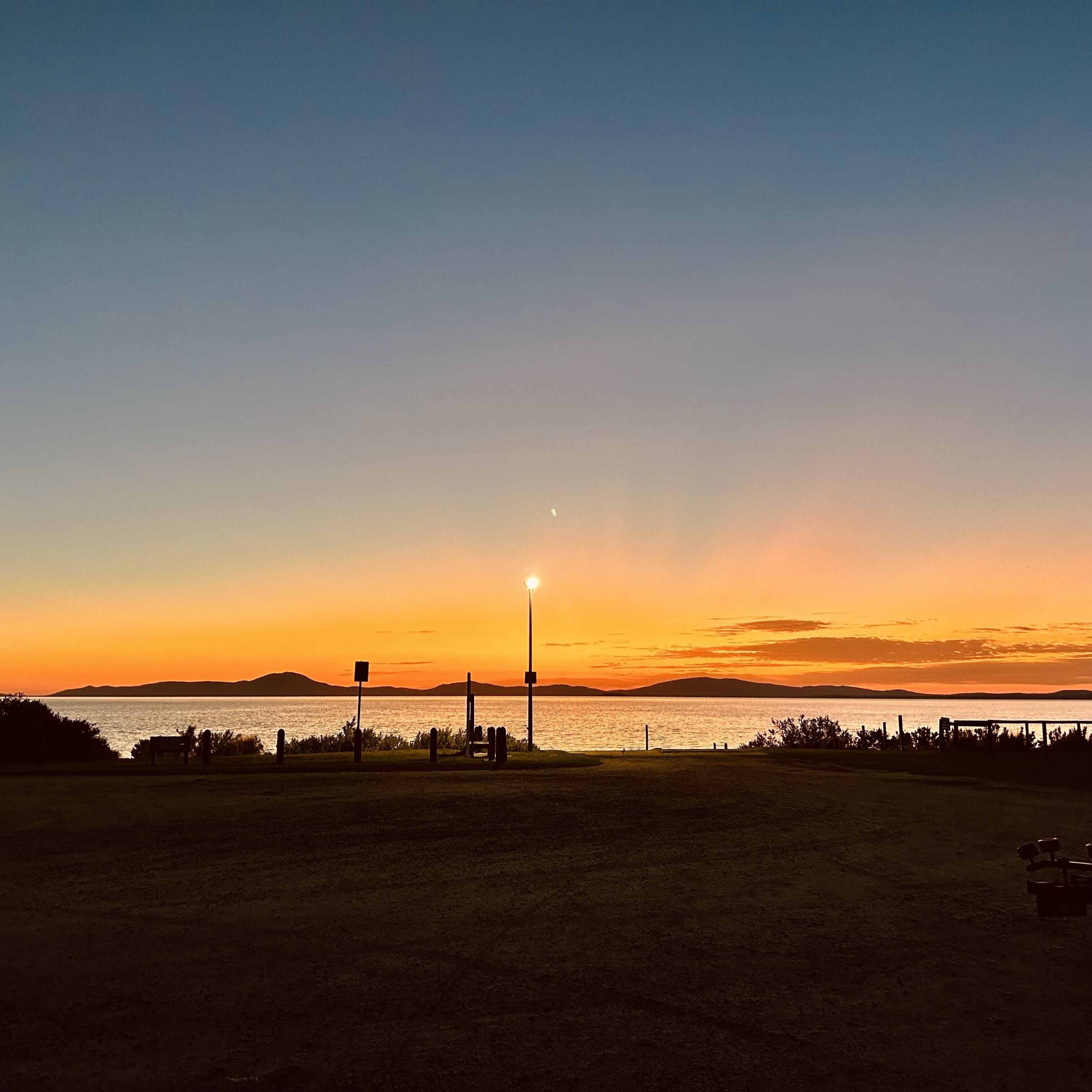 A sunset view over a body of water with a park area in the foreground.