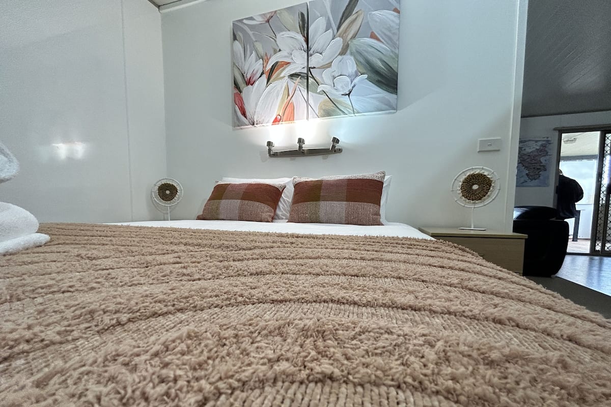 A bedroom with a large bed, a wall-mounted light, and a painting.