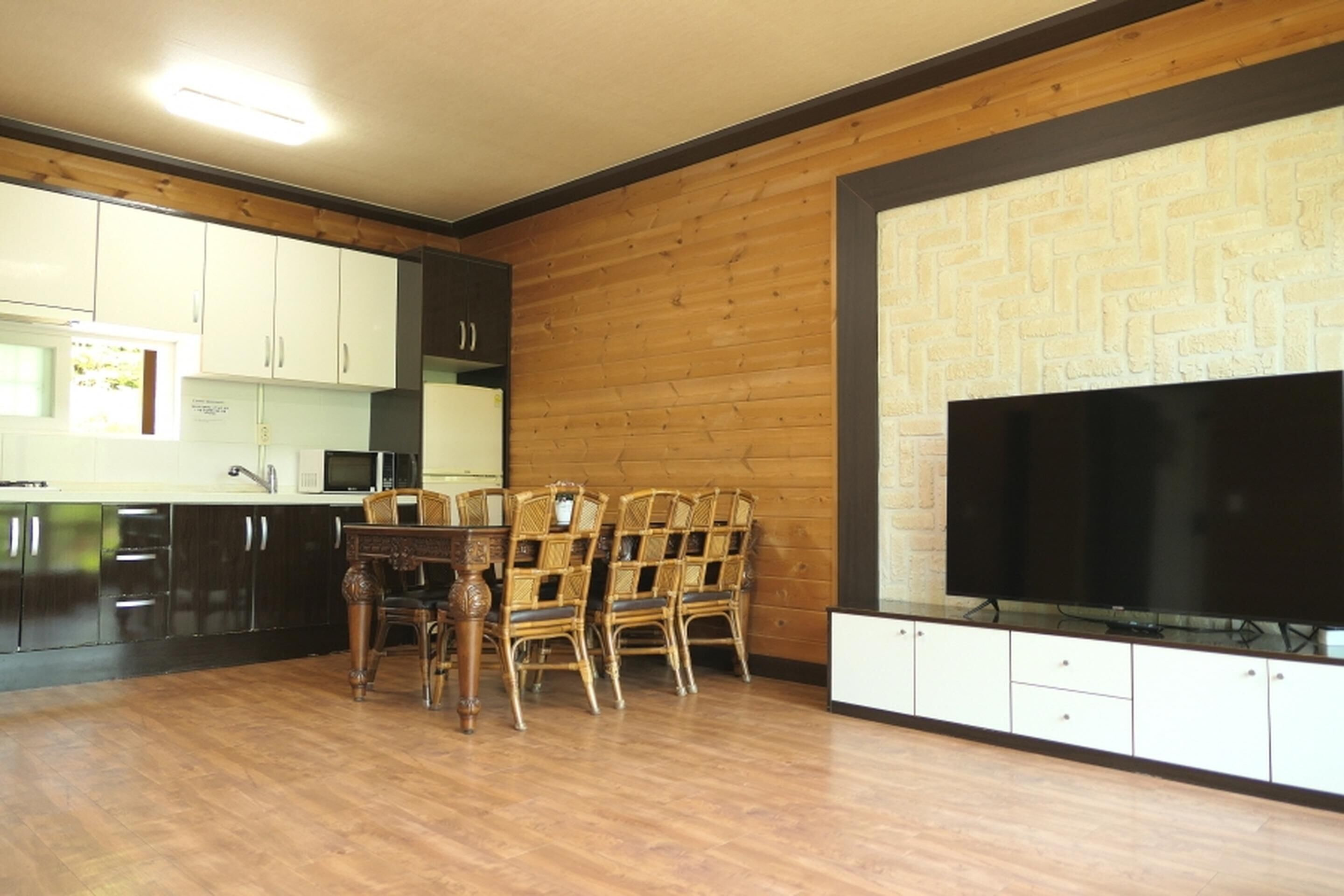 Una cocina con armarios de madera, una mesa de comedor con sillas y un televisor de pantalla plana montado en la pared.