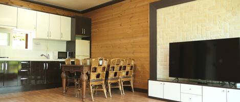 Una cocina con armarios de madera, una mesa de comedor con sillas y un televisor de pantalla plana montado en la pared.