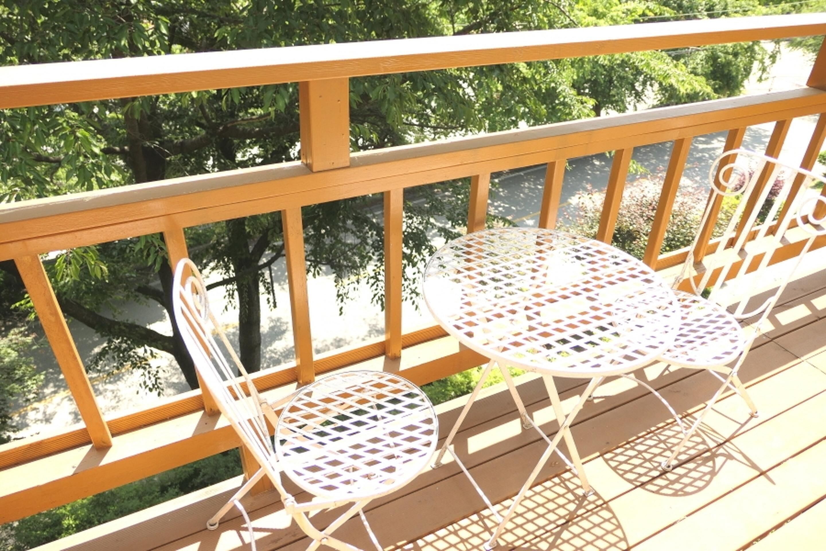 Una terraza de madera con dos mesas y sillas de metal blanco.