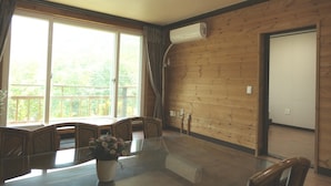 Una habitación con interior de madera, un ventanal con cortinas, una mesa con sillas y un equipo de aire acondicionado en la pared.