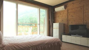 Un dormitorio con una cama, televisor y ventana con vista a un balcón y follaje.