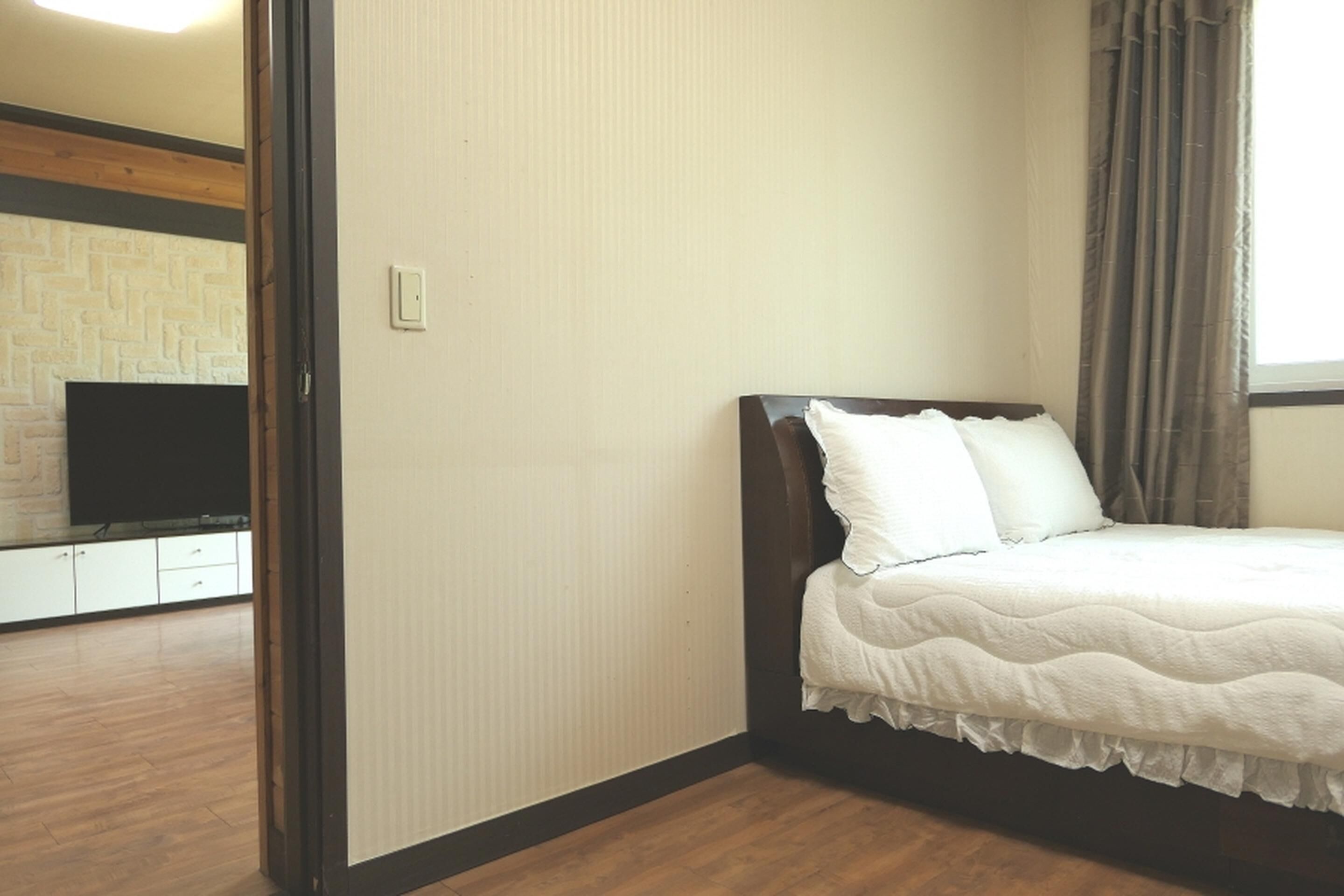 A bedroom with a bed, a television, and a wooden floor.