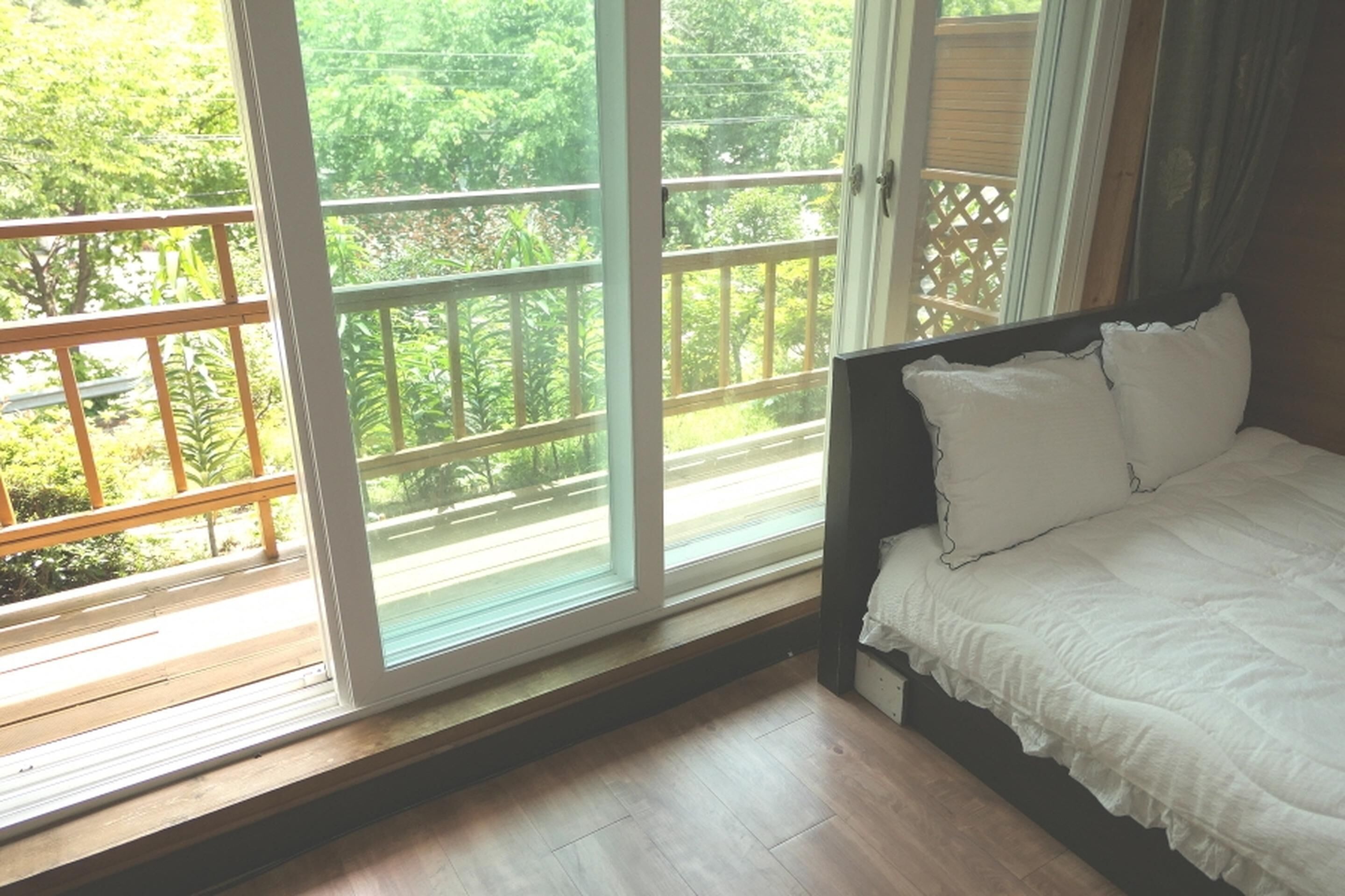 A bedroom with a large window, a wooden floor, and a bed with white bedding.