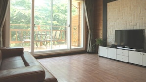Una sala de estar con un sofá, un televisor sobre un mueble bajo y un ventanal corredizo que da a un área exterior con terraza de madera.