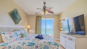Une chambre à coucher avec un lit, un ventilateur de plafond, une télévision et une vue sur l’océan par la fenêtre.