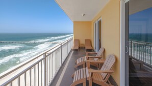 Un balcon avec des chaises et une table en bois, d’où l’on peut admirer l’océan, ses vagues et, au loin, une jetée.