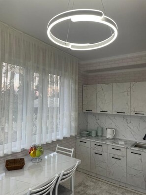 Une cuisine moderne avec des meubles de rangement en marbre blanc, une table à manger blanche et un luminaire circulaire original.