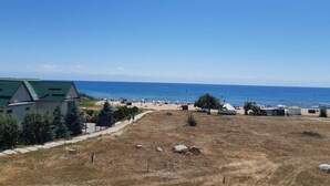 A coastal area with a beach, a fenced property with a green-roofed building, and a clear blue sky.