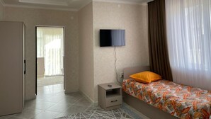 A bedroom with a bed, a TV mounted on the wall, a nightstand, and a door leading to another room.