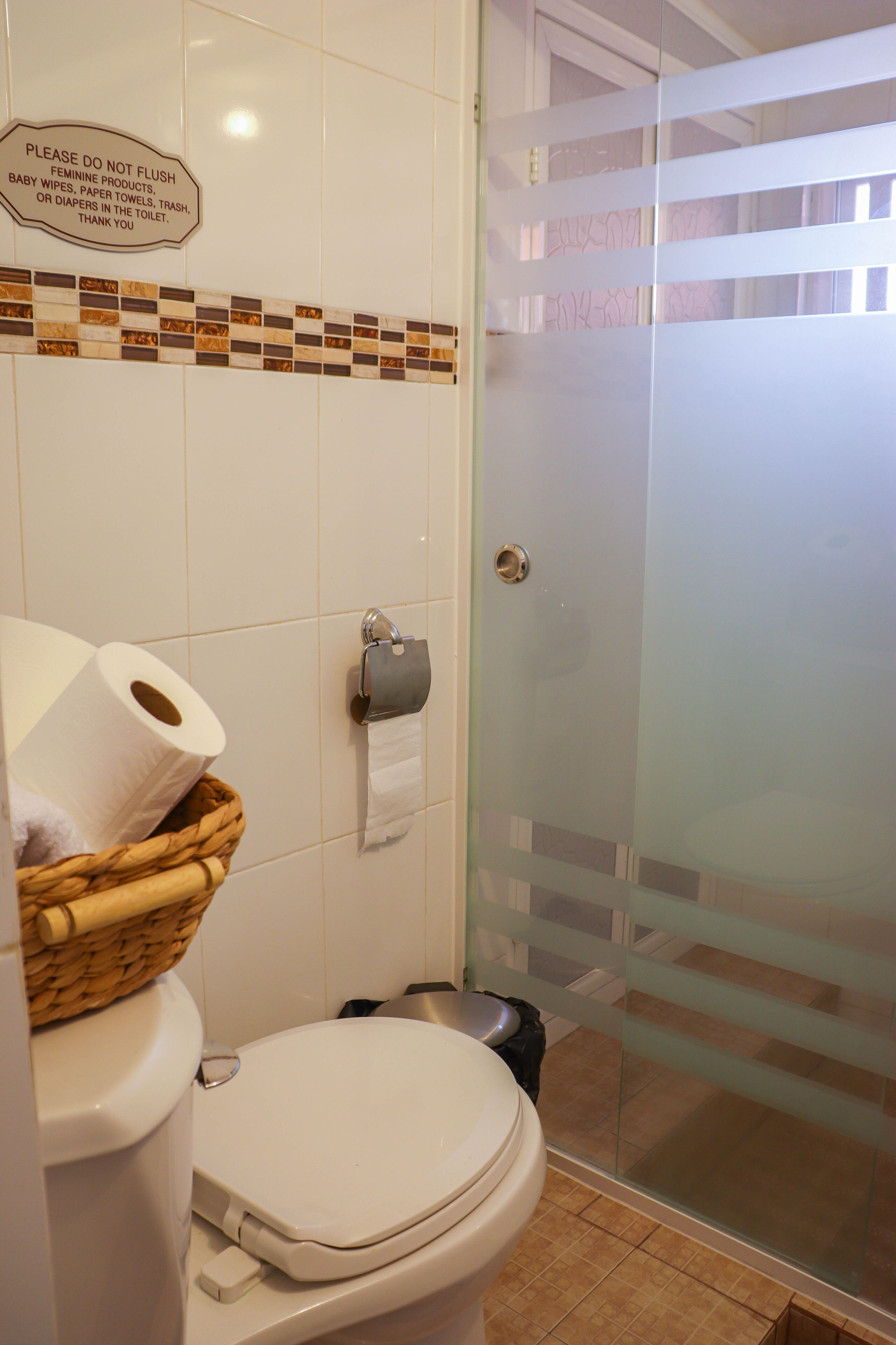 A bathroom with a toilet, a basket of toilet paper, a hand dryer, and a sign instructing not to flush feminine products.