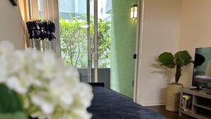 A modern bedroom with a large bed, a TV, and a view of greenery outside. - Lush 1 bd Koreatown w/ FREE parking & In-Unit laundry (Commerce)