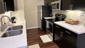 A modern kitchen with dark cabinetry, stainless steel appliances, and a white countertop. - Lush 1 bd Koreatown w/ FREE parking & In-Unit laundry (Commerce)