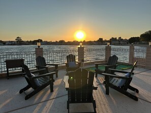 A deck with outdoor seating and a view of the sunset over a body of water.