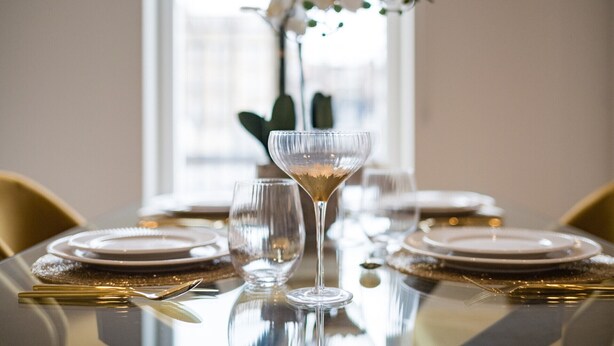 Ein Esstisch ist gedeckt mit Tellern, Besteck und einem Martini-Glas.