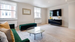 Ein modernes Wohnzimmer mit einem grünen Sofa, einem Glastisch, einer schwarzen Unterhaltungseinheit und einem großen Flachbildfernseher.
