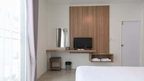 Een moderne hotelkamer met een bed, een aan een houten paneel bevestigde televisie, een klein plankje met handdoeken, een prullenbak en een raam met gordijnen.