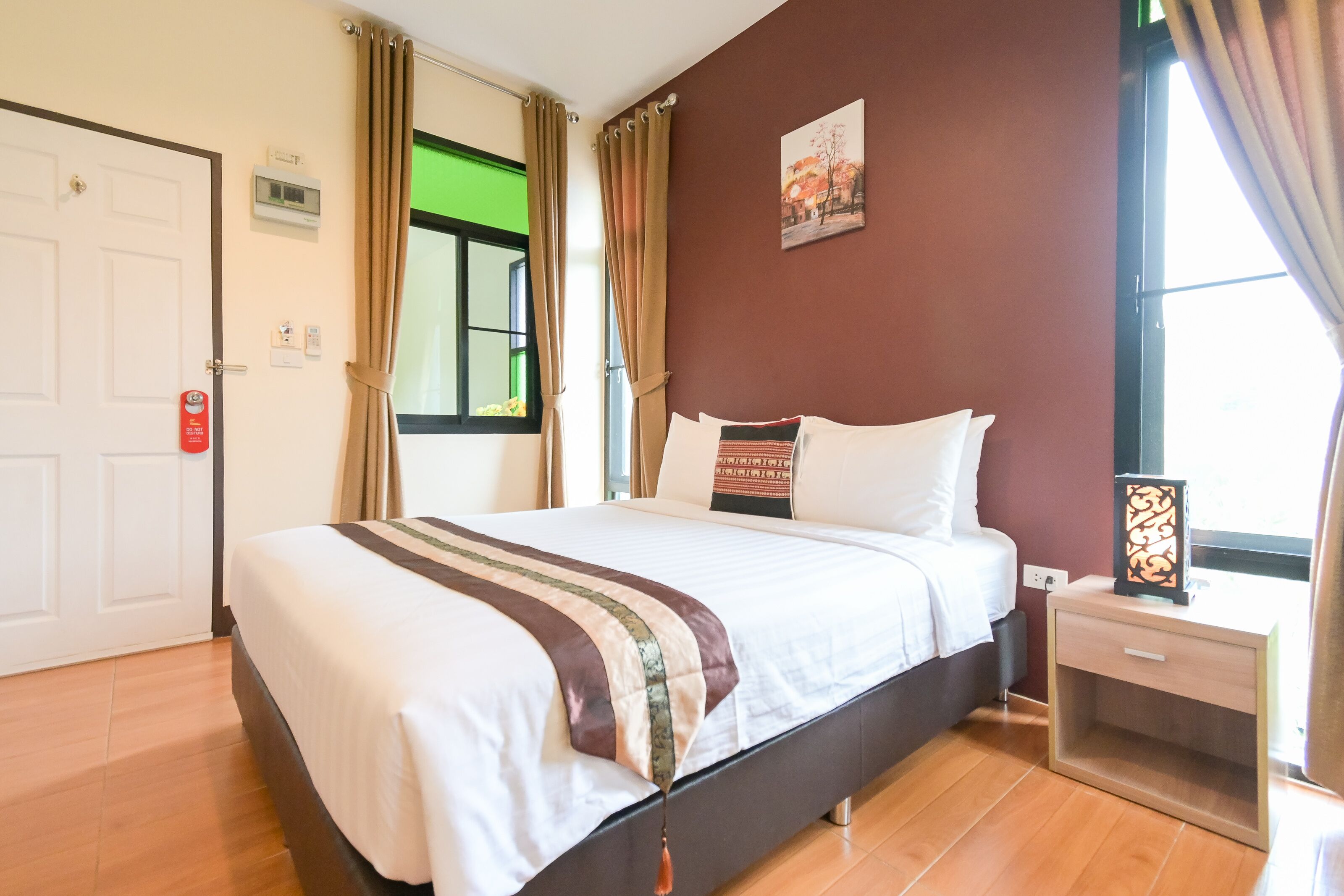 Een net opgemaakt bed met een gestreept dekbedovertrek, een nachtkastje met een decoratief object, en een raam met gordijnen.