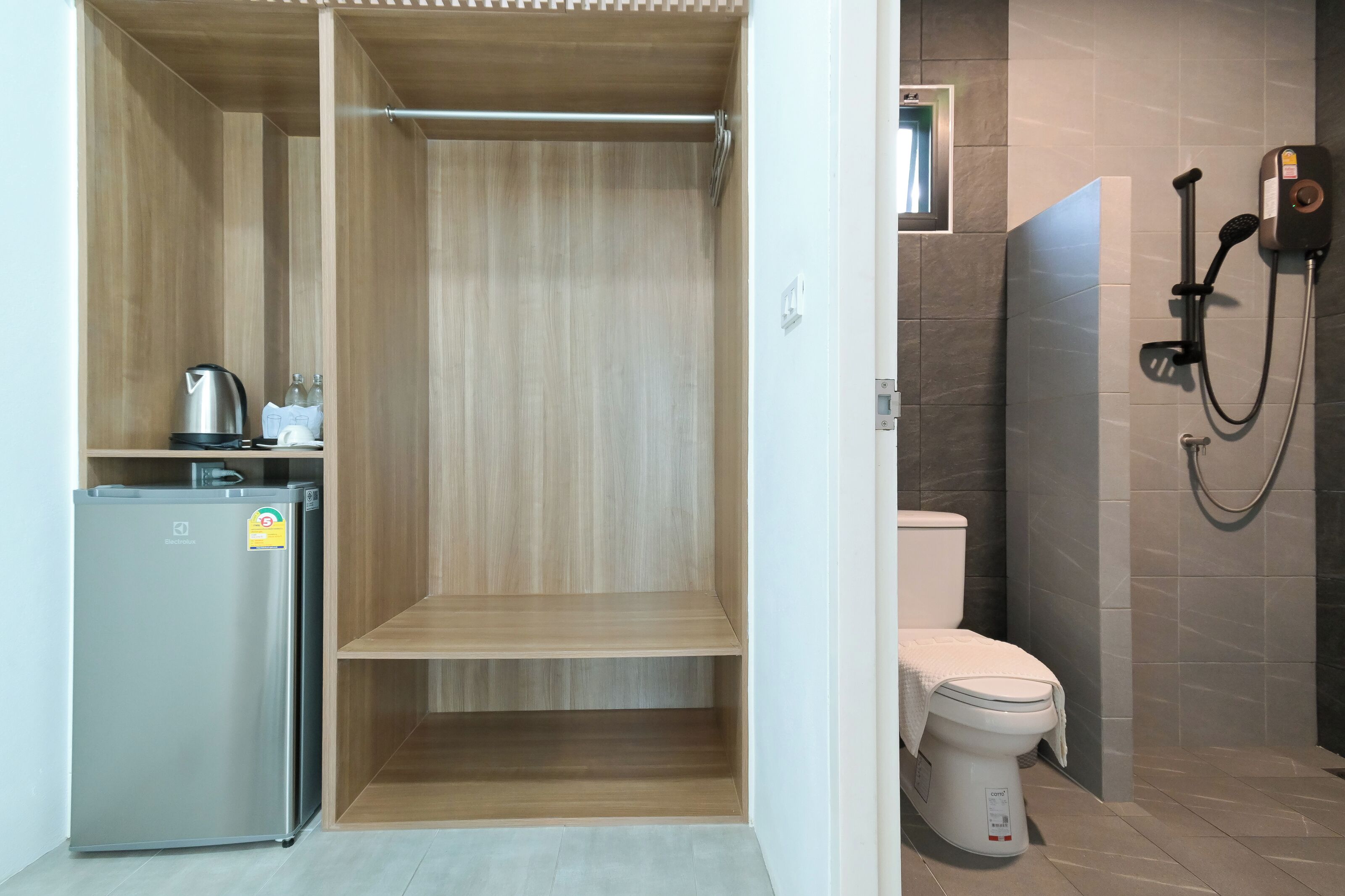 A compact bathroom with a shower, toilet, and a small refrigerator.