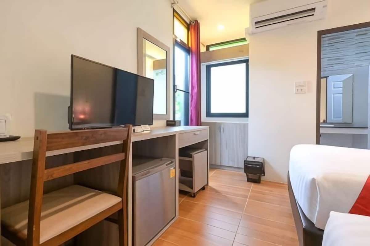 Een hotelkamer met een bed, een bureau met een televisie, een kleine koelkast en een raam met gordijnen.