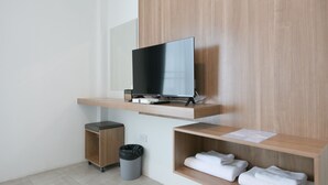 Een moderne hotelkamer met een bevestigde televisie, een kleine prullenbak en netjes opgevouwen handdoeken op een plank.