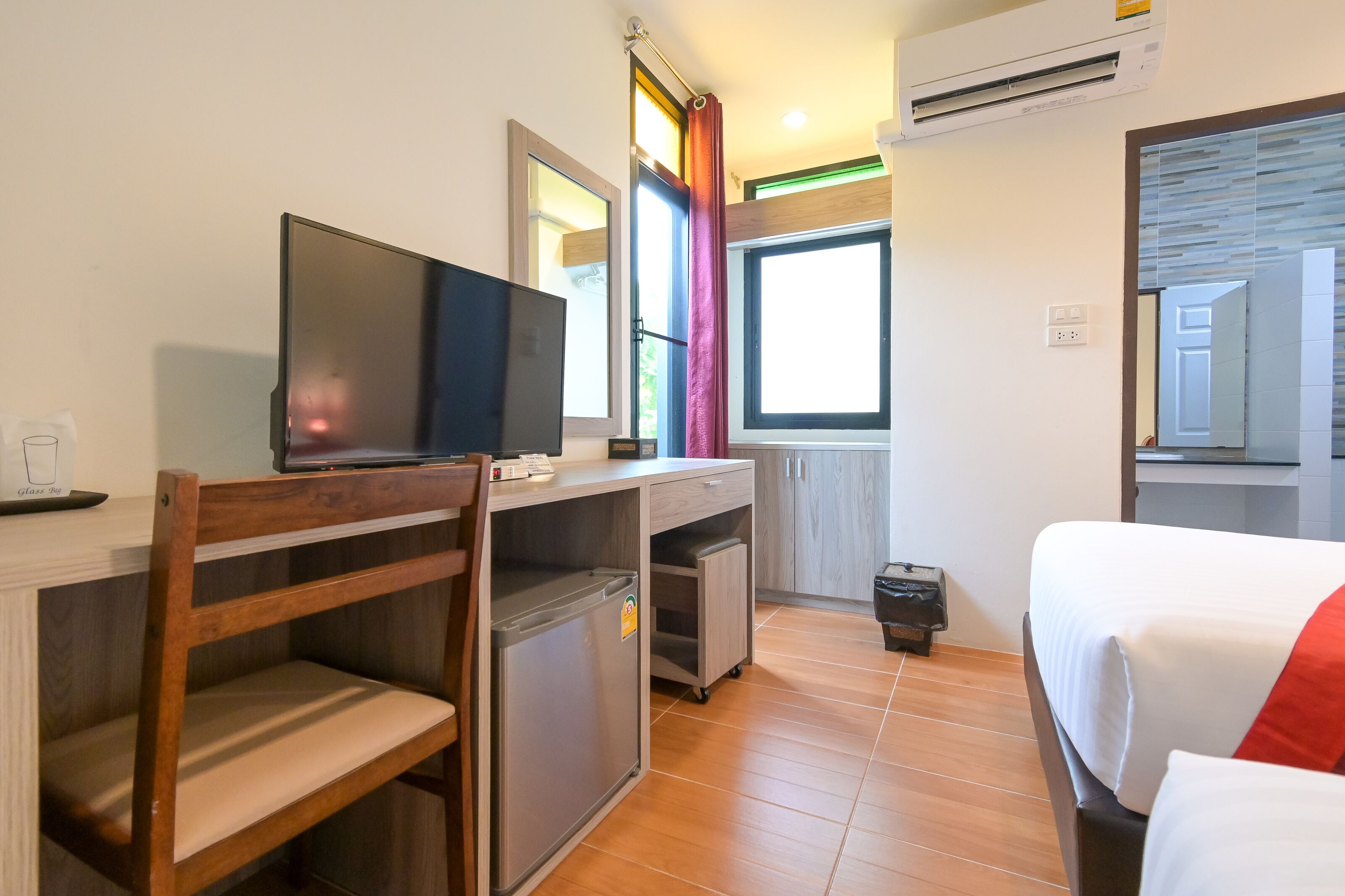 A hotel room with a bed, a desk with a television, a small refrigerator, and a window with curtains.