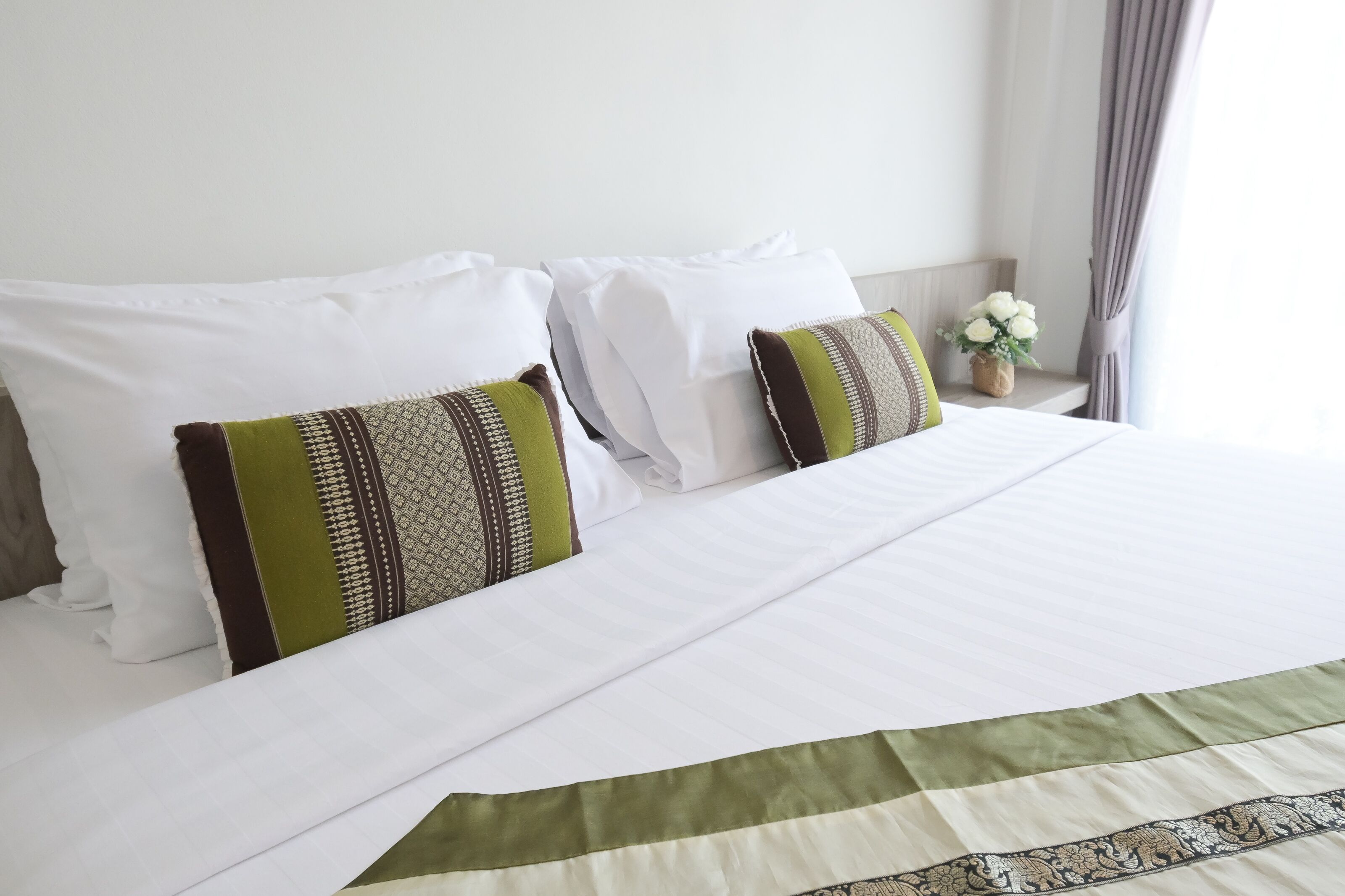 A neatly made bed with white linens and two decorative pillows with green and brown patterns.