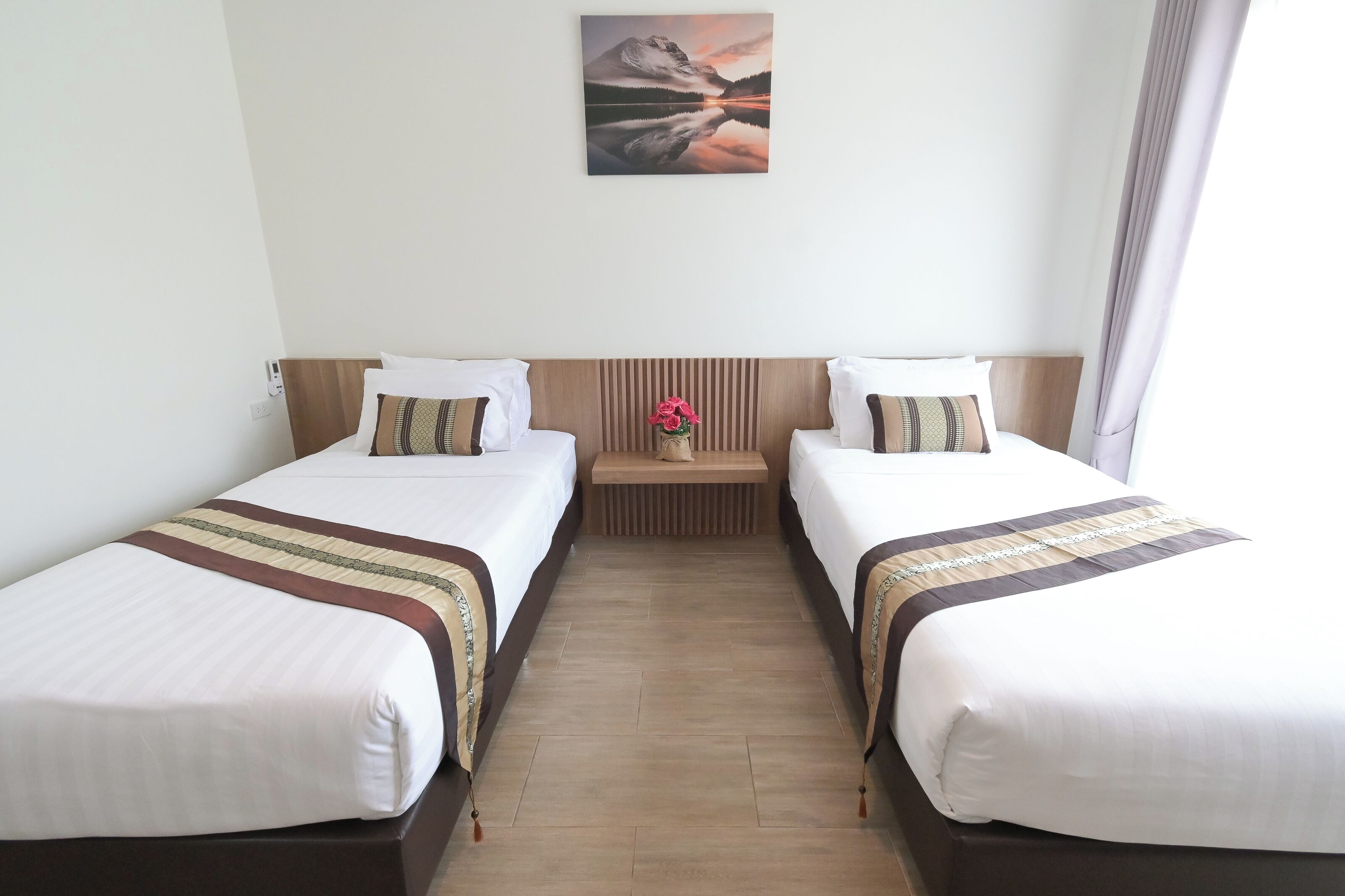 Habitación de hotel con dos camas, cabecera de madera, mesita de noche con un florero y un cuadro en la pared.