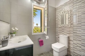Une salle de bain dotée d’une grande fenêtre, d’un lavabo, de toilettes et d’un miroir décoratif.