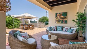 An outdoor patio with wicker furniture, a dining area, and a large painting on the wall.