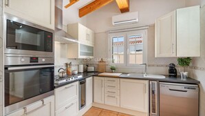 A modern kitchen with white cabinets, stainless steel appliances, a wooden ceiling, and a window with a view.