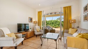 A living room with a TV, sofas, a glass coffee table, and yellow curtains.
