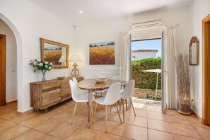 Un coin repas avec une table en bois et des chaises blanches, un buffet en bois et deux tableaux accrochés au mur.
