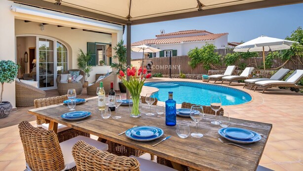 An outdoor pool area with a wooden table set for dining, surrounded by wicker chairs and lounge chairs.